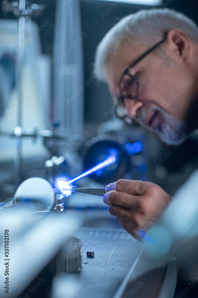 Portrait of Focused Middle Aged Engineer in Glasses Working with High Precision Laser Equipment, Usi