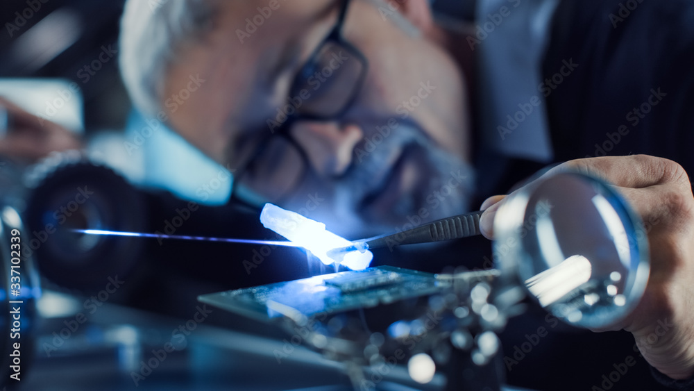 Close-up Portrait of Focused Middle Aged Engineer in Glasses Working with High Precision Laser Equip