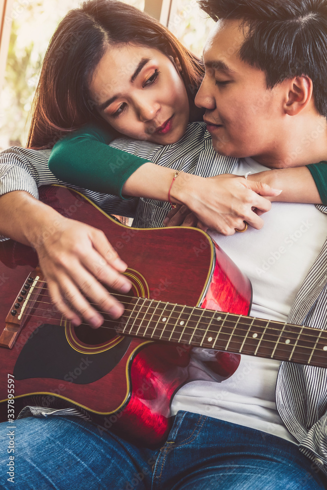 Young Asian Couple Plays Guitar and Sing Song in Living Room at Home Together. Music and Lifestyle c
