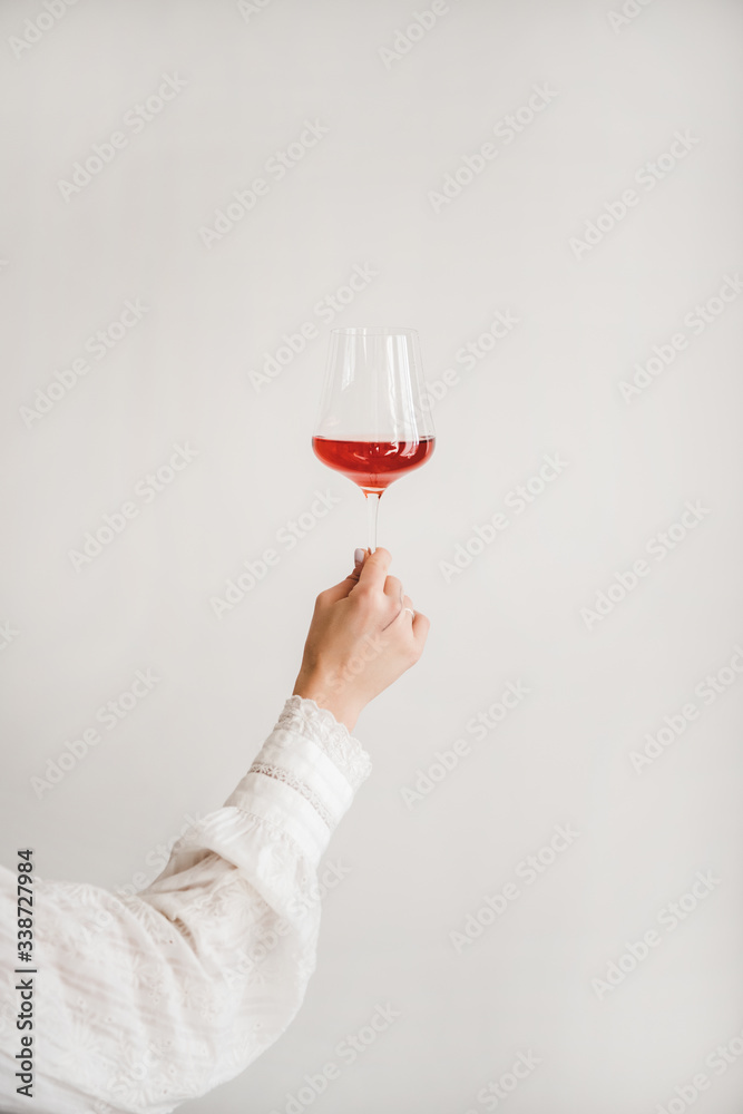 Womans hand holding glass of rose wine over white wall background. Wine shop, wine tasting, bar, win