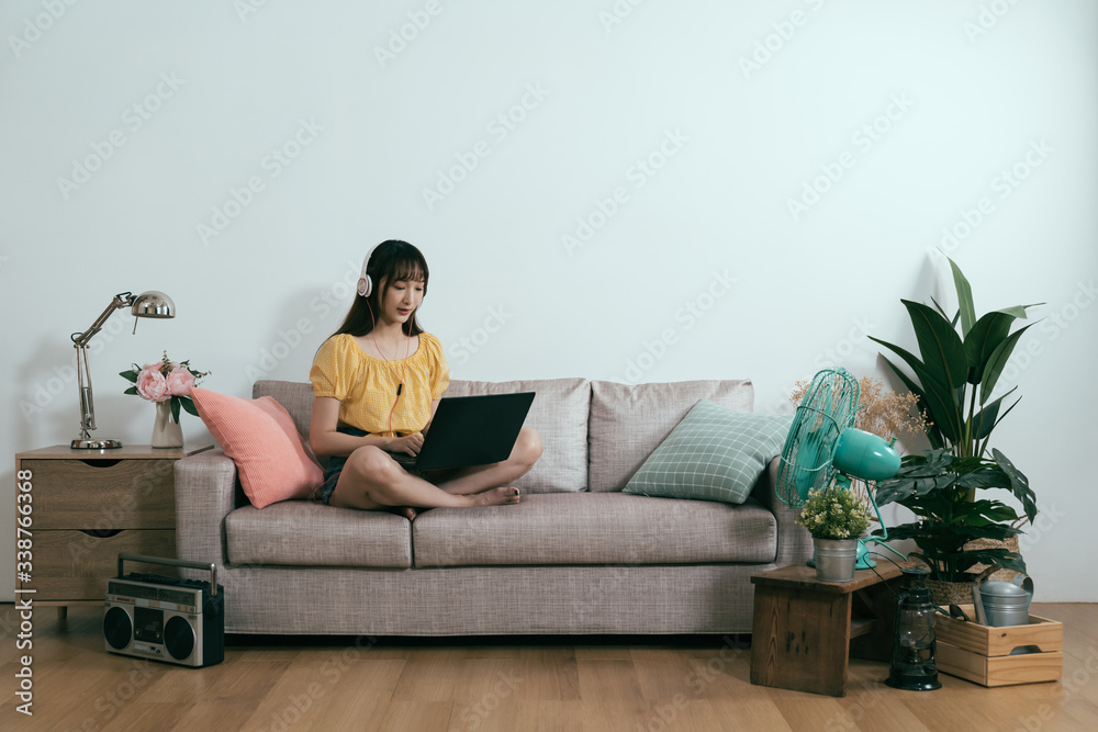 asian girl slacking off using laptop and earphones in living room. korean young lady is binge-watchi