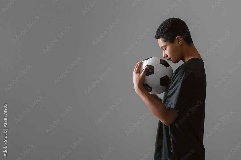 Young African-American football player on grey background