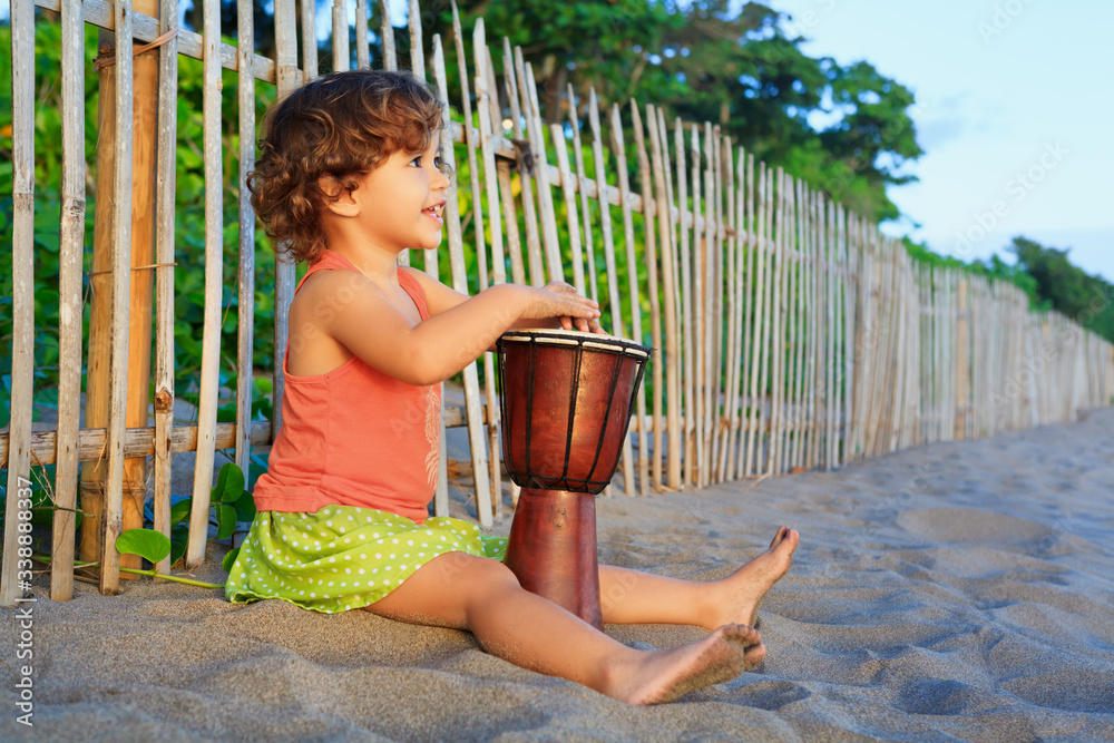 快乐的小女婴用传统的非洲手鼓djembe演奏民族音乐，欣赏日落