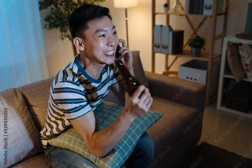 快乐的男人喝着一瓶啤酒看电视，晚上欢呼。年轻快乐的亚洲日本人g