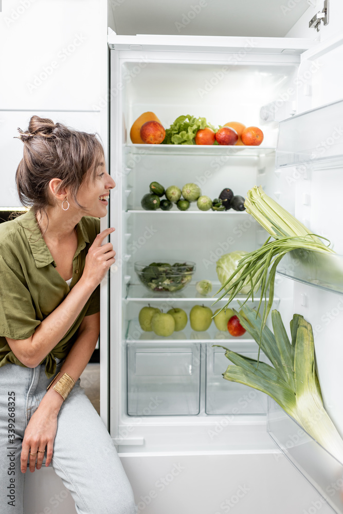 一位年轻女子坐在厨房桌子上，冰箱旁边摆满了新鲜健康的食物