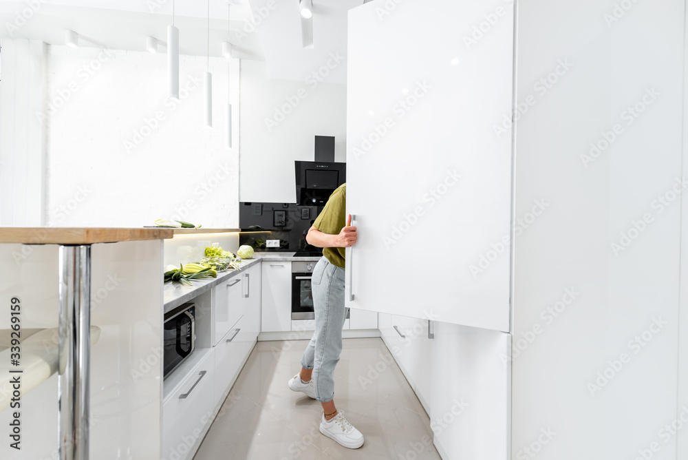 女人在家里的现代厨房里烹饪健康食品，看着冰箱，尽情享受