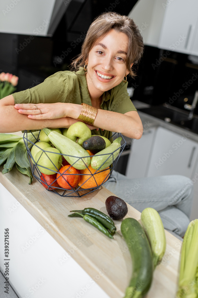 Portrait of a young and cheerful woman with healthy raw food on the kitchen at home. Vegetarianism, 