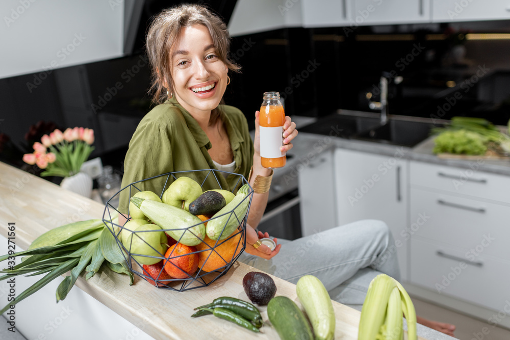一位年轻开朗的女士喝着果汁，坐在厨房里吃着健康的生食的画像