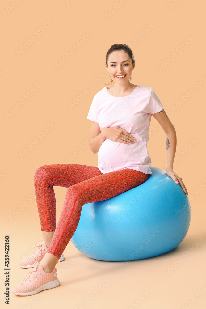 年轻孕妇在彩色背景下用健身球做运动