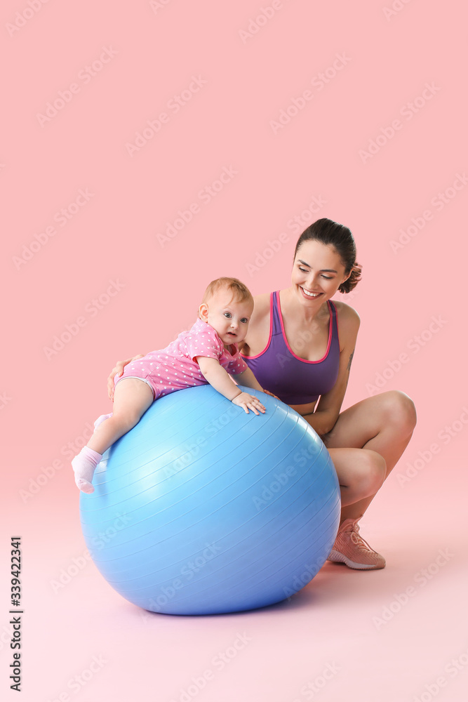 年轻的运动型妈妈和她的宝宝在彩色背景下用健身球做运动