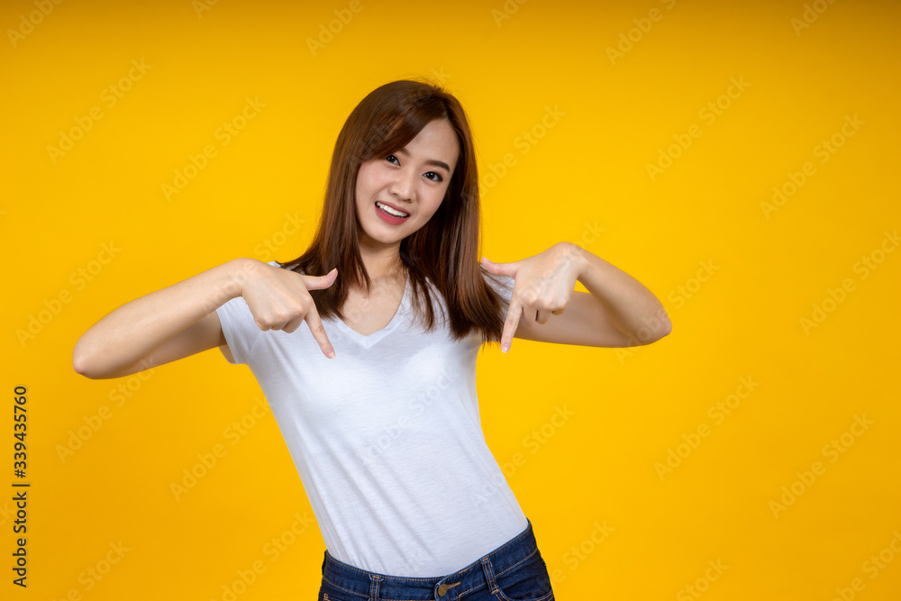 年轻优雅的亚洲女性微笑着指着黄色背景上隔离的空复制空间