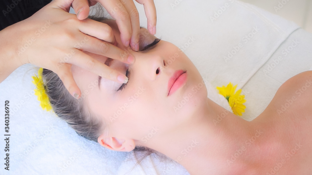 放松的女人躺在水疗床上，接受按摩治疗师的面部和头部按摩水疗治疗