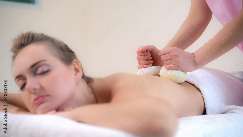 按摩治疗师在豪华水疗中心为躺在水疗床上的女性进行草药敷治疗