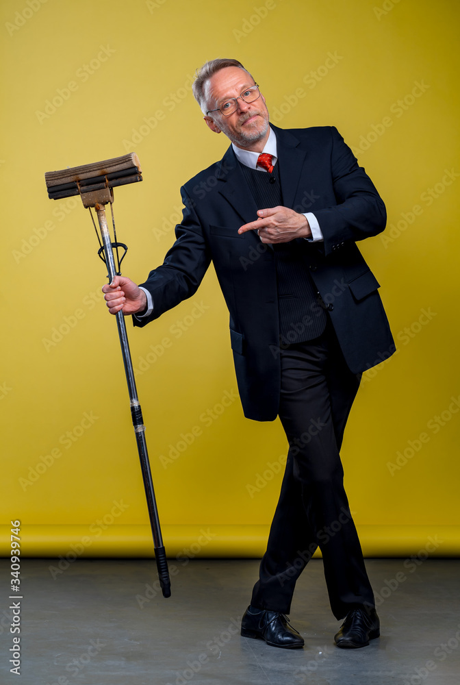 Senior man in suit holding a boom. Manager man pointing at mop in studio.
