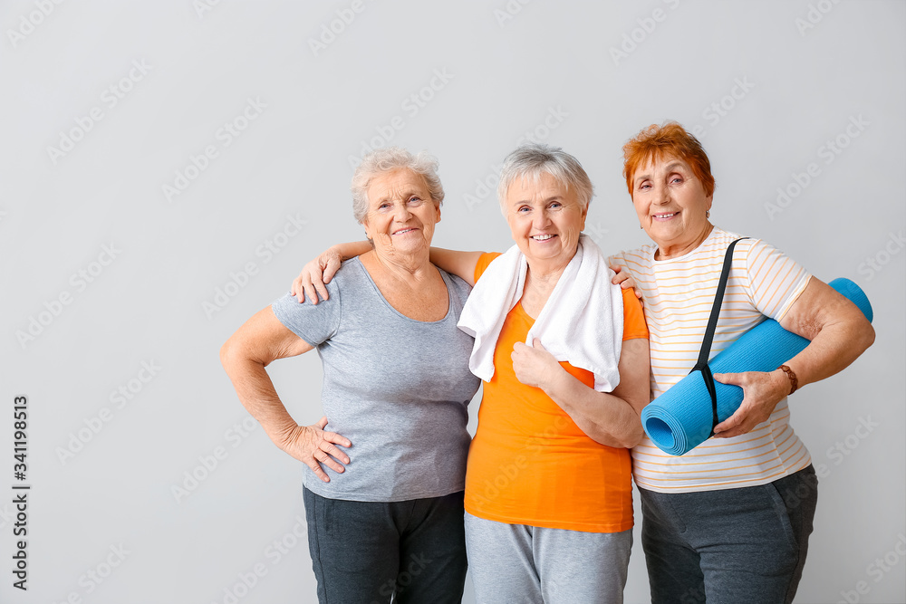 Happy elderly women with yoga mat on light background