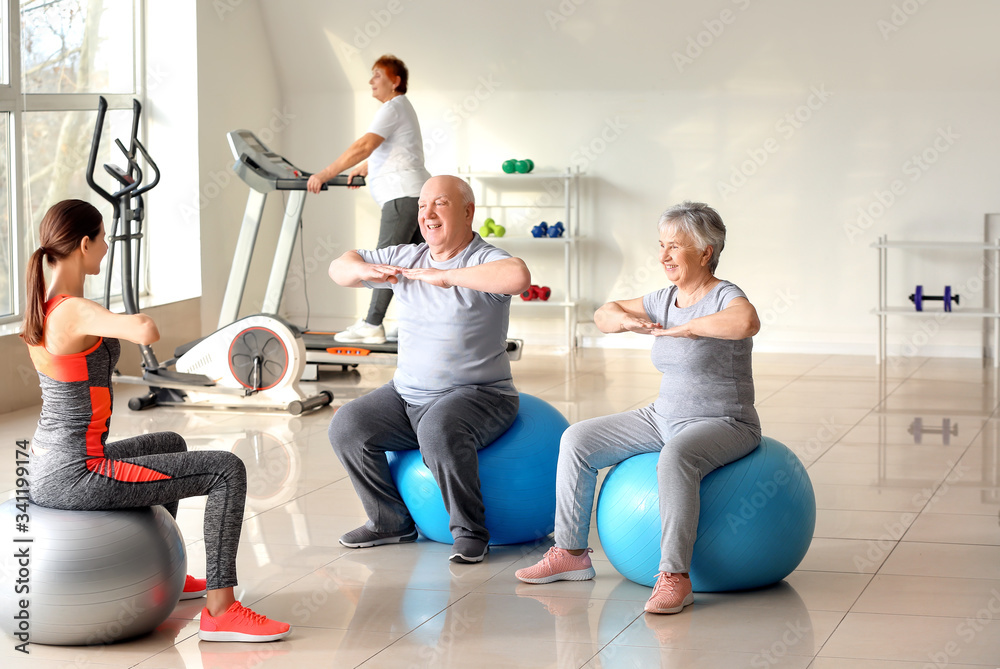 Young trainer exercising with elderly people during training in gym