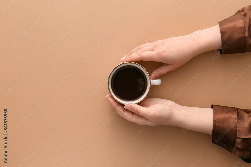 女性双手，彩色背景上有一杯热咖啡，俯视图