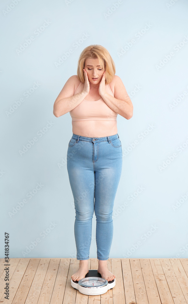 麻烦的超重女性，体重秤在彩色背景上。减肥概念