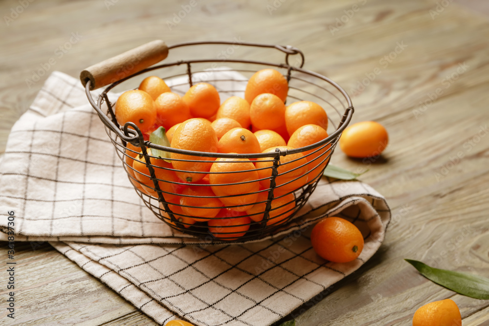 Basket with tasty kumquat fruit on wooden background