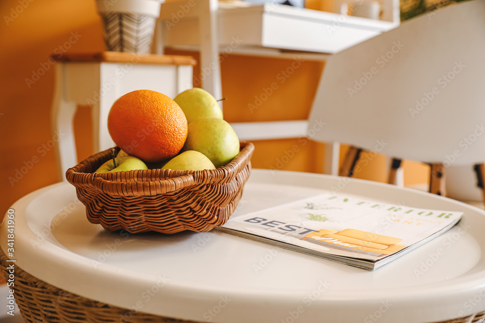 Wicker basket with fresh fruits and fashion magazine on table in room