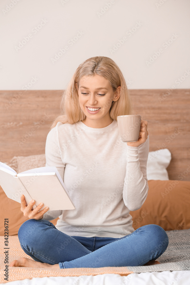 美丽的年轻女子在家看书时喝茶