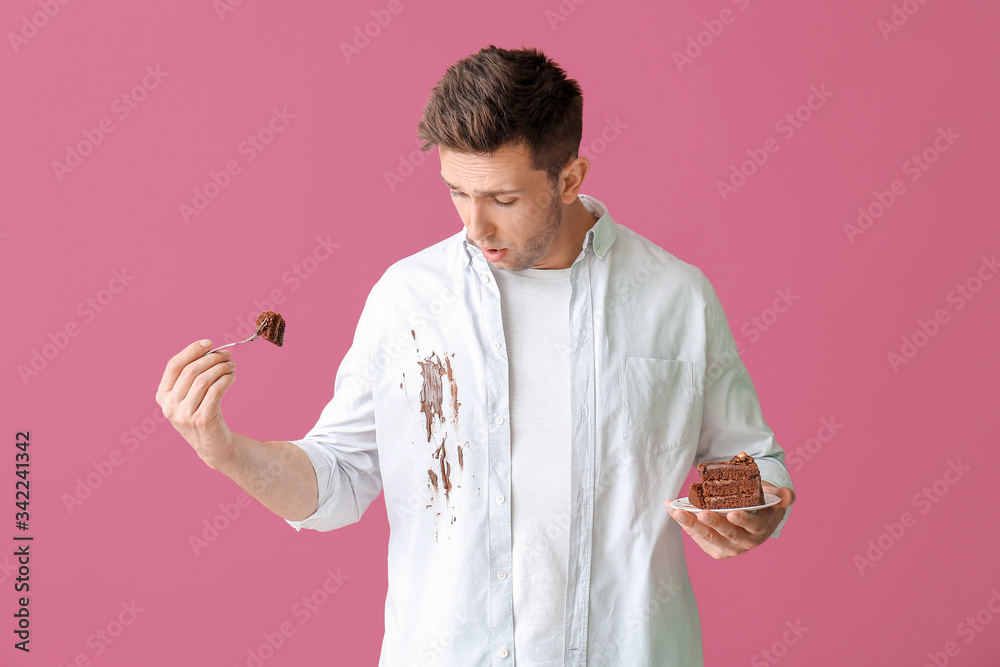 穿着脏衣服的麻烦男子在吃彩色背景的巧克力蛋糕