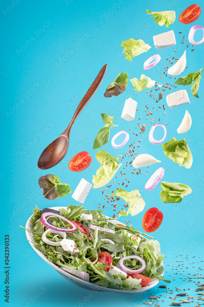 蓝色背景下的飞行沙拉。希腊沙拉：红番茄、奶酪、生菜、洋葱和种子