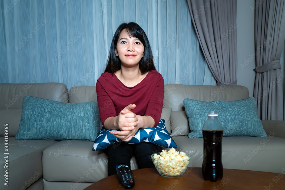 年轻的亚洲女性看电视悬疑电影或新闻，看起来很开心，很放松，吃着爆米花