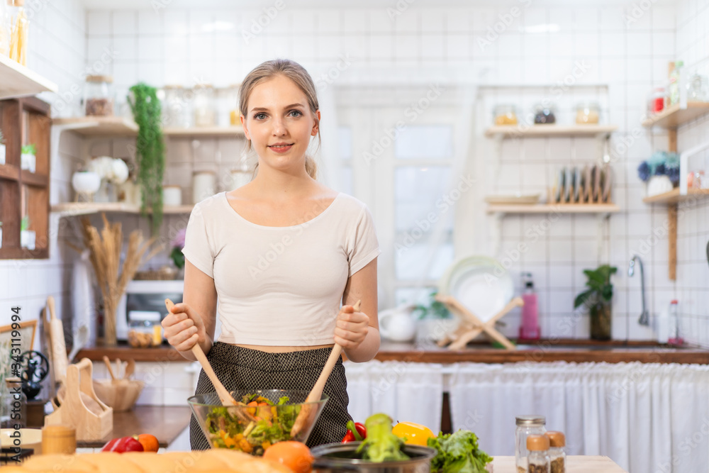 Lovely cute Caucasian girl making green vegetable salad in kitchen at home. Portrait of young woman 