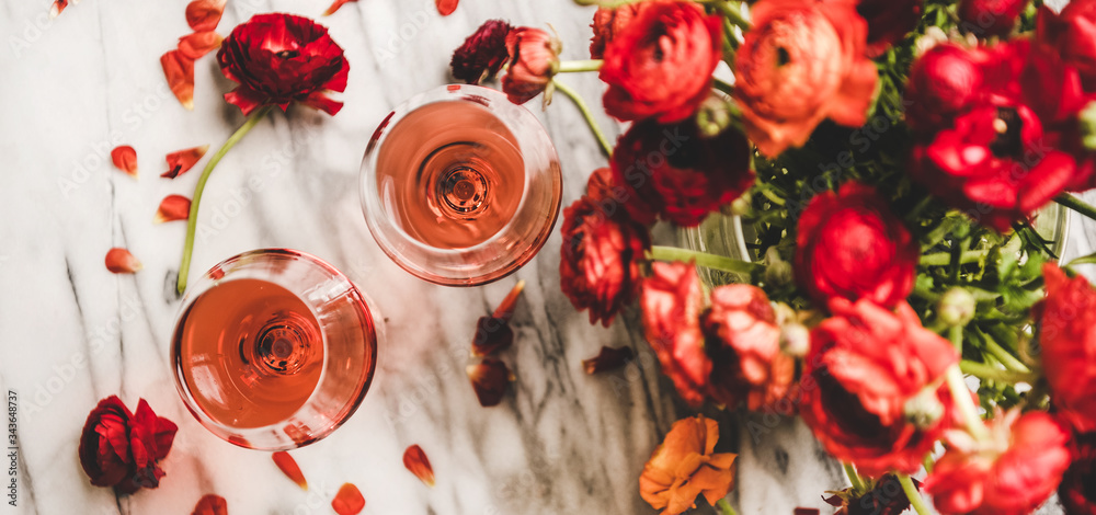 平躺在玻璃杯中的玫瑰酒和白色大理石背景下的红色春天花朵
