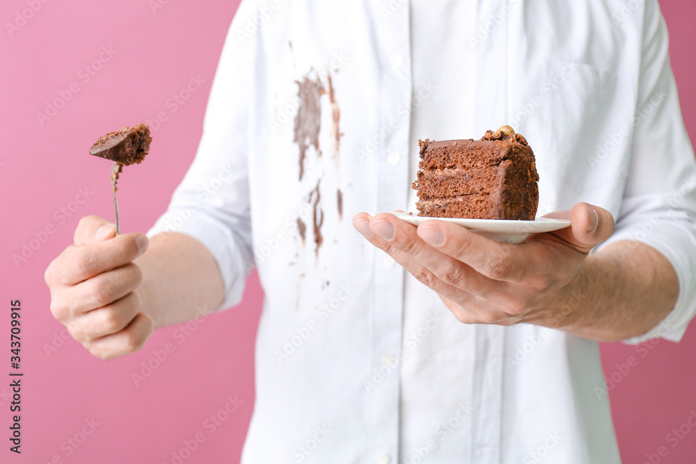 一名穿着脏衣服的男子正在吃彩色背景的巧克力蛋糕，特写镜头