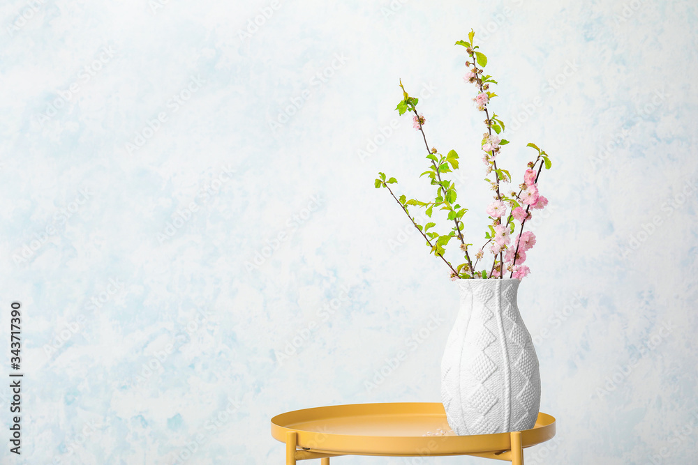 在浅色背景下，桌上摆放着美丽盛开的树枝的花瓶