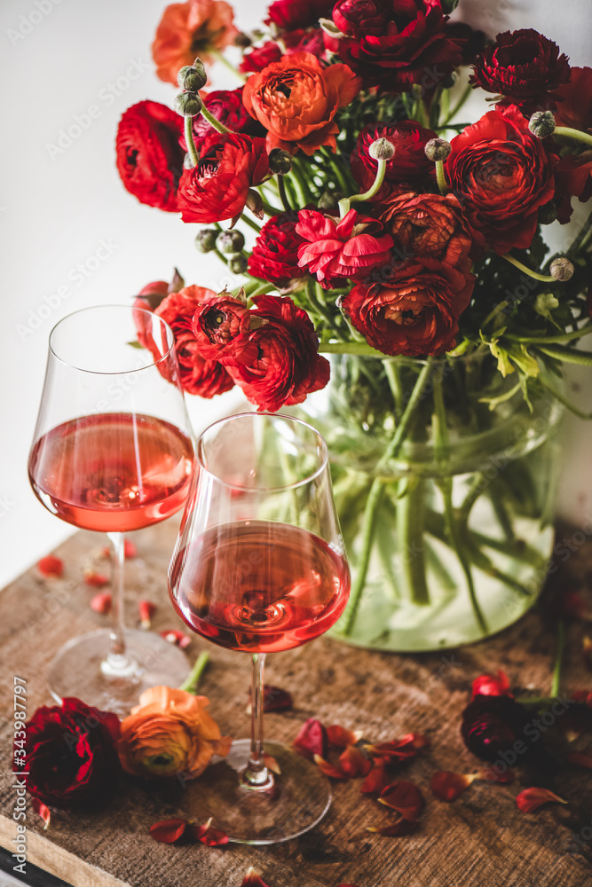 装在玻璃杯里的玫瑰酒和红色的春天花朵在质朴的木桌背景下绽放。获胜