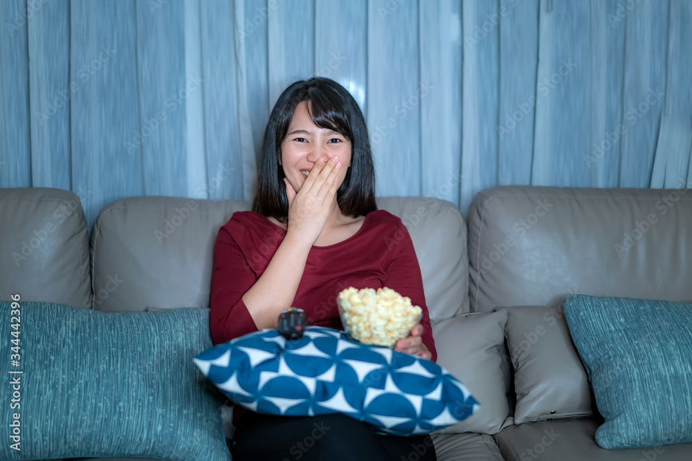 年轻的亚洲女性看电视悬疑电影或新闻，看起来既开心又有趣，吃着爆米花