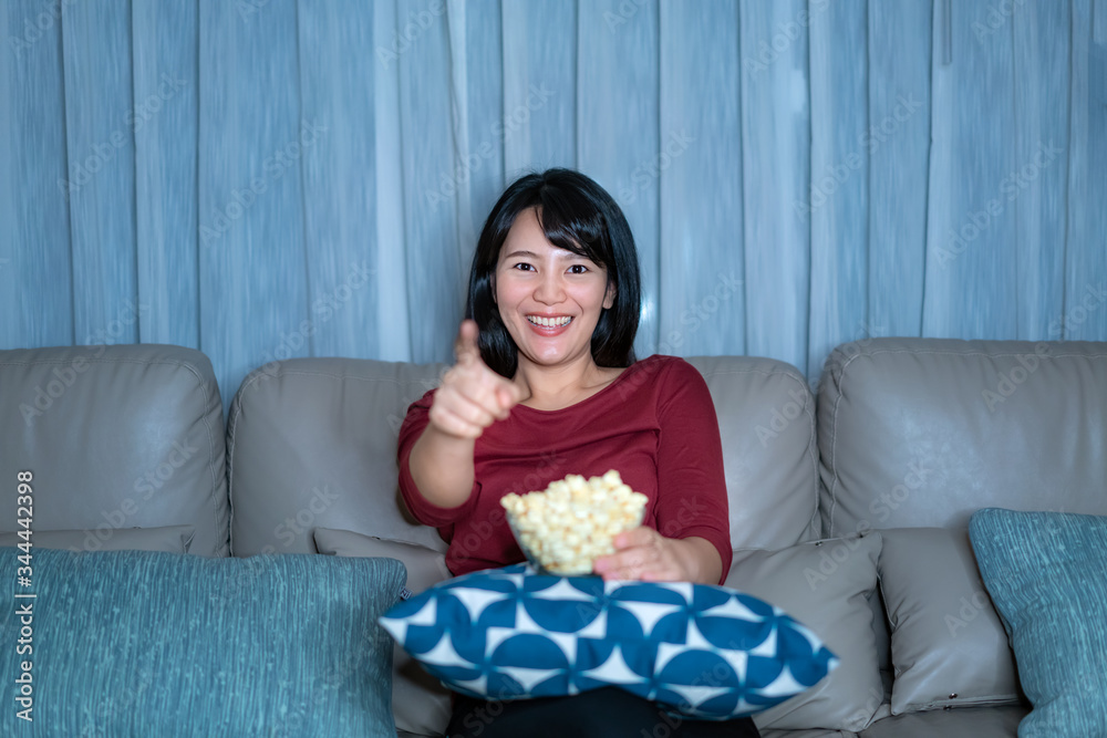 Young asian woman watching television suspense movie or news looking happy and funny and eating popc