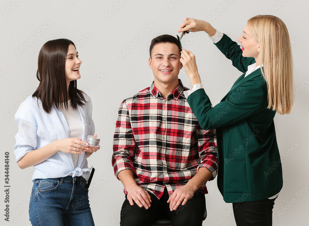Young hairdressers working with client against light background