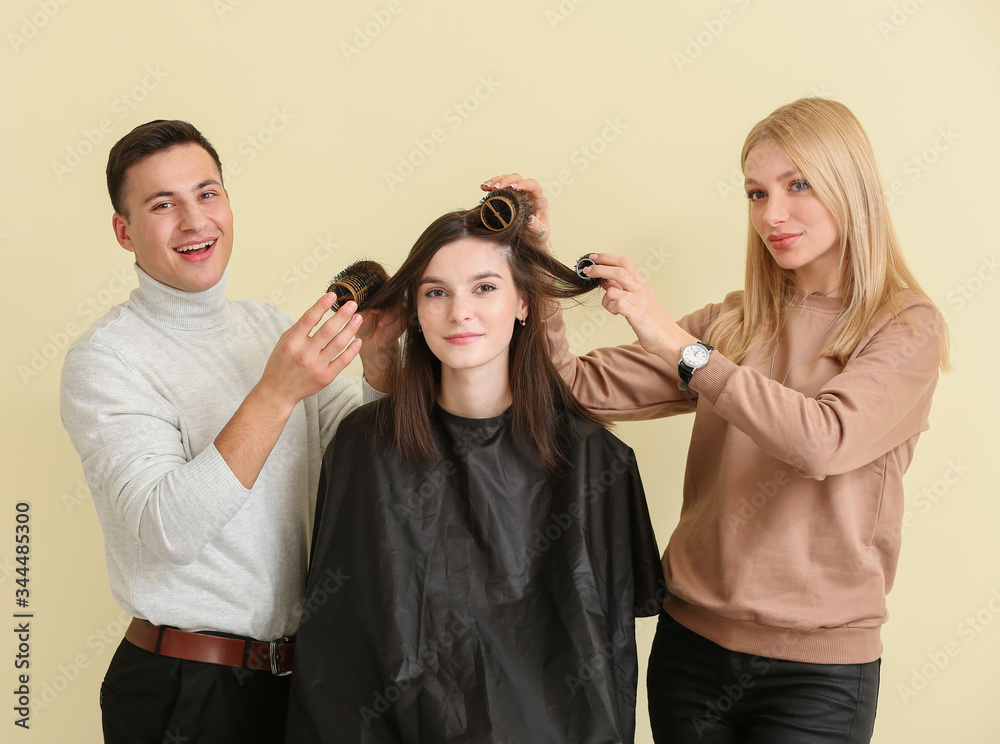 Young hairdressers working with client against color background