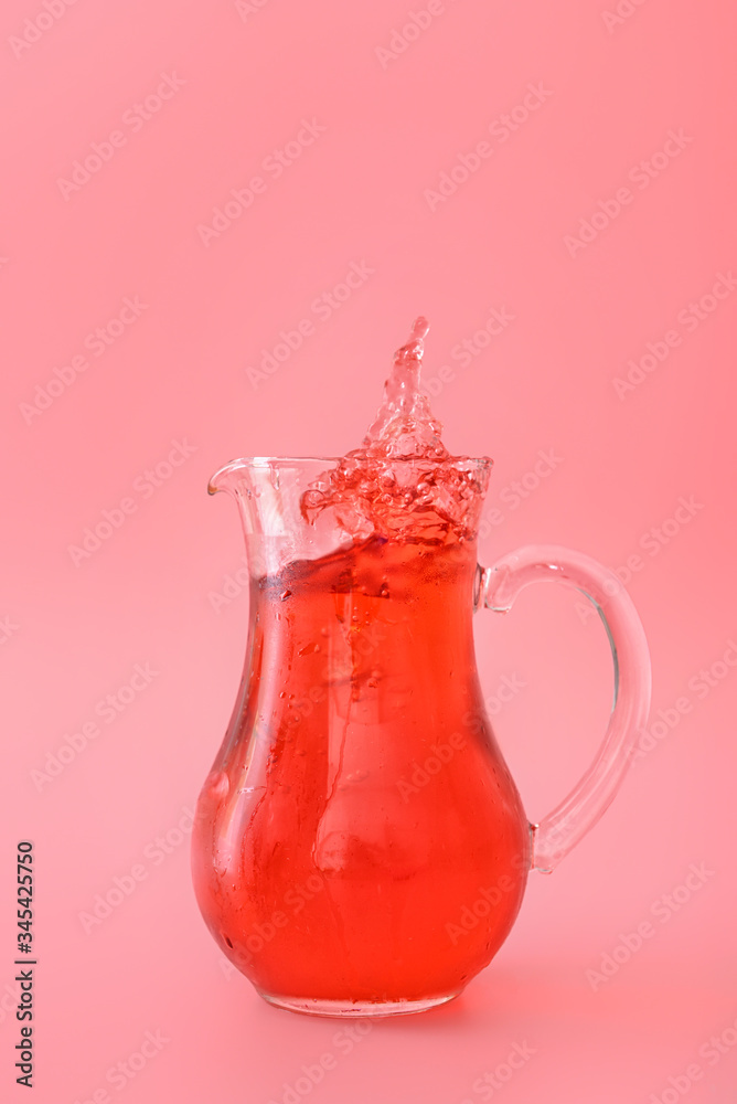 Jug of tasty cold ice tea with splash on color background
