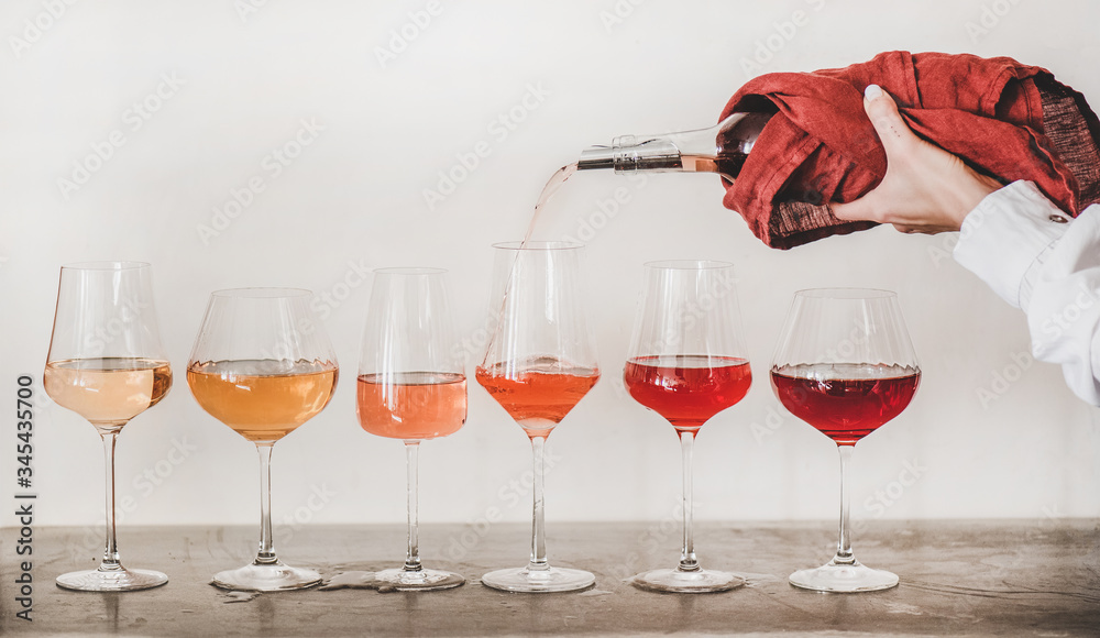 带梗玻璃杯中的玫瑰色葡萄酒排成一行，女人们用手将葡萄酒从瓶子倒到gl