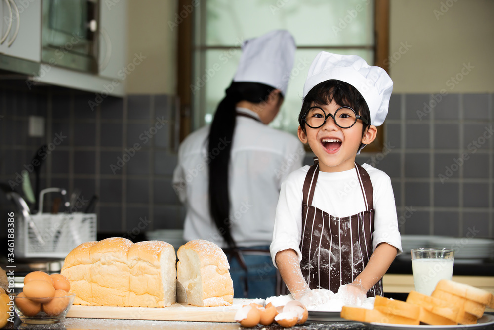 快乐可爱的亚洲小男孩，穿着围裙，在家厨房准备烤面团
