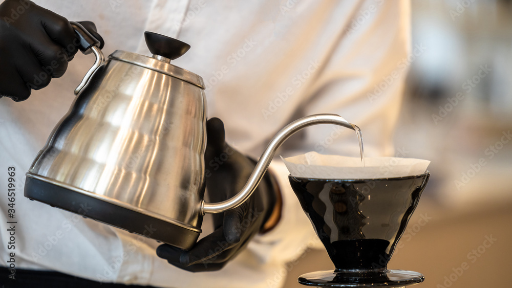 穿着白衬衫的咖啡师把热水洒出来，从银茶壶里准备过滤后的咖啡，变成漂亮的bla