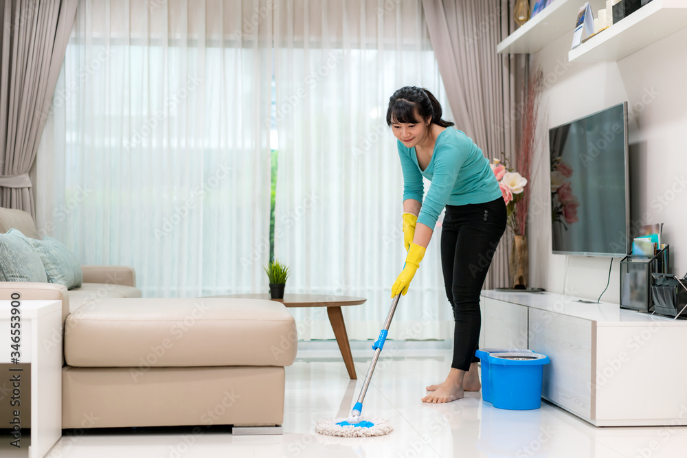 迷人的年轻亚洲女性在S期间在家打扫卫生，在客厅拖地