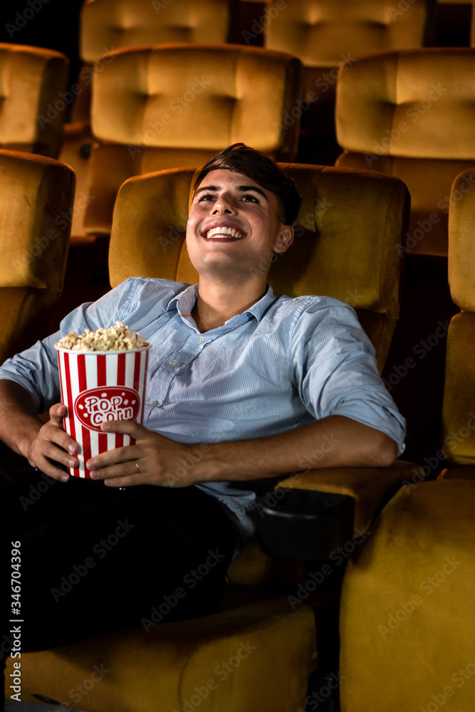 一个年轻人在电影院看电影时微笑着拿着爆米花