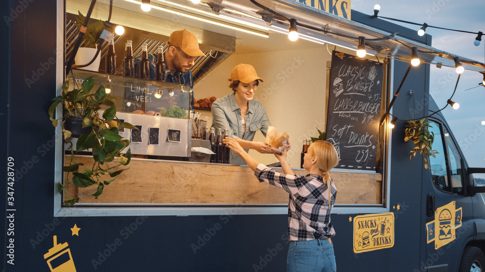 食品卡车员工向一位快乐的年轻女性分发一个新鲜制作的汉堡和一杯软饮料。街头