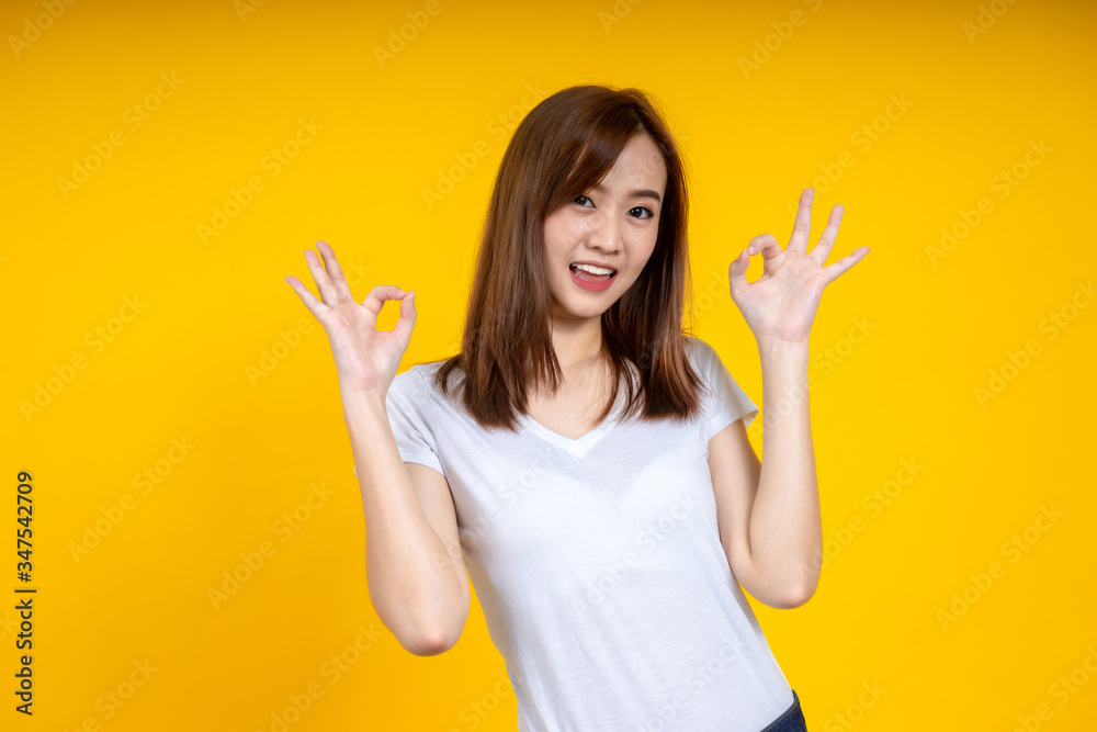 年轻优雅的亚洲女性微笑着，用手在黄色背景上做了隔离的OK标志