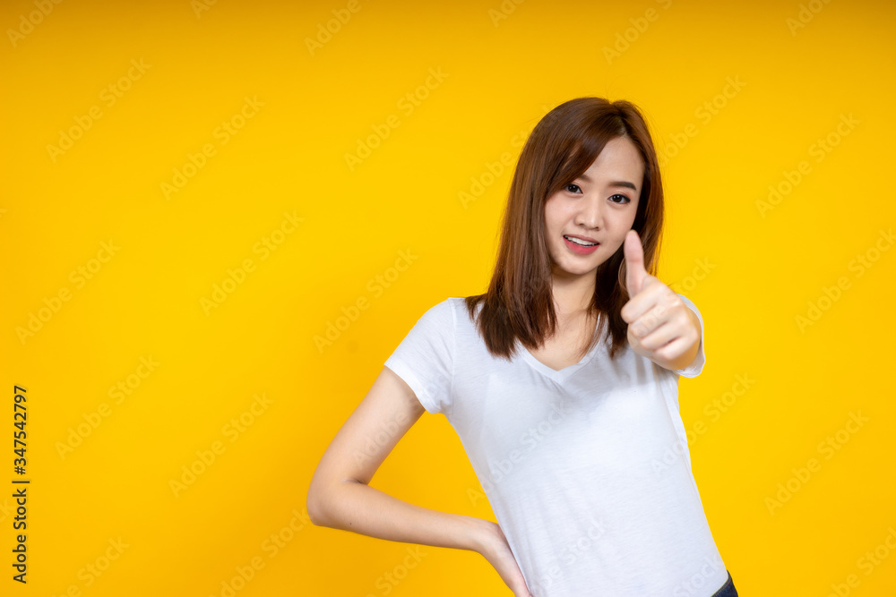 年轻优雅的亚洲女性微笑着展示拇指向上的黄色背景上隔离的复制空间