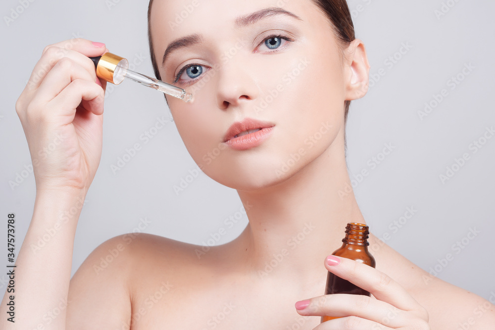 美丽的深色皮肤女士用移液管在脸上涂抹化妆品油的特写。美容疗法总结