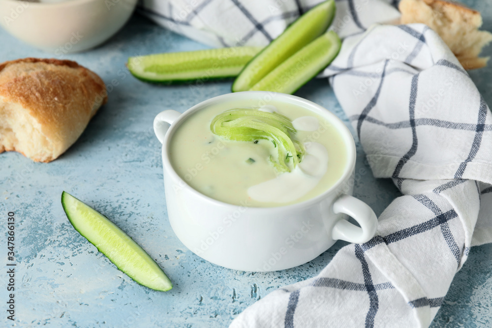 Pot with cold cucumber soup on color background
