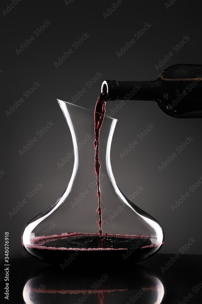 在深色背景下将美味的葡萄酒从瓶中倒入玻璃杯