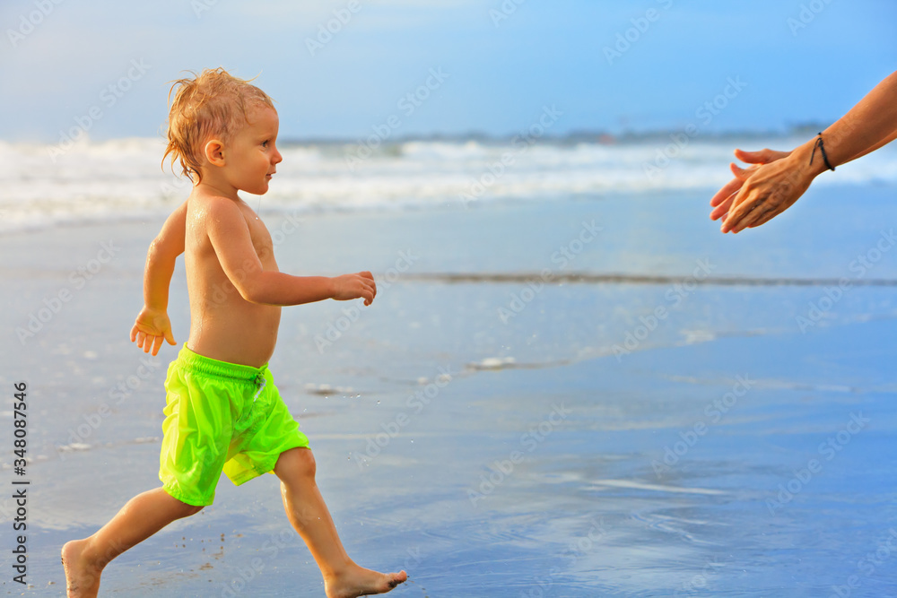 快乐的一家人在热带海滩度假胜地玩得很开心。有趣的婴儿在冲浪边的水池旁奔跑